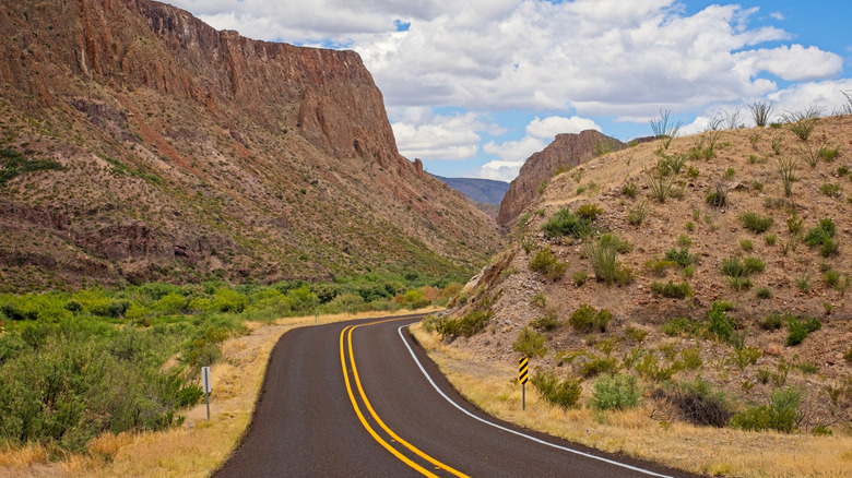 road winding through desert hills and rocky cliffs, sky and clouds in the background