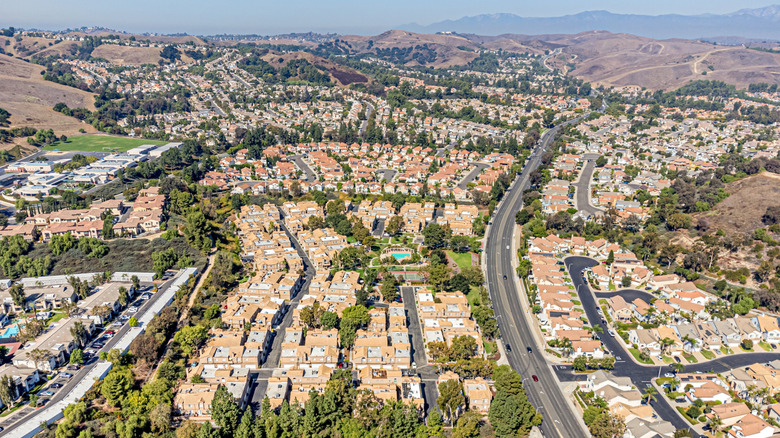 An aerial view of houses, trees, and roads with hills in the background