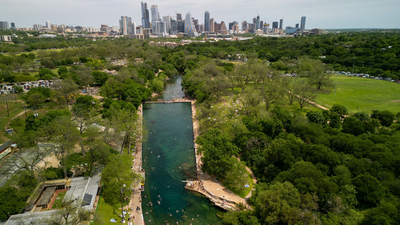 An aerial view of Barton Springs Pool in Zilker Metropolitan Park on a sunny day with Austin skyline in the background in Texas, USA