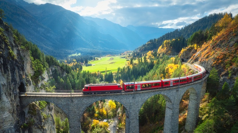 Aerial view of modern red train on Landwasser viaduct in alpine mountains