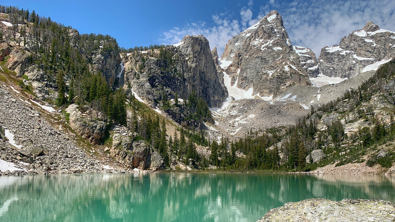 Snow-lined, forested mountains surrounding the blue waters of Delta Lake in Grand Teton National Park
