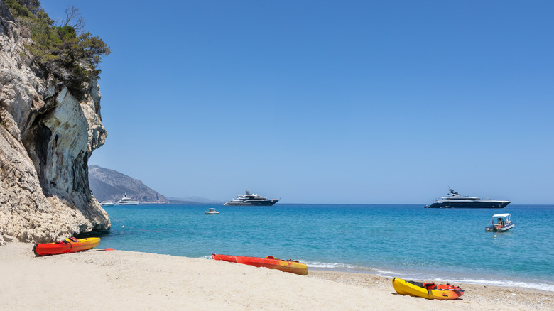 kayaks on a beach and luxury yachts on the horizon