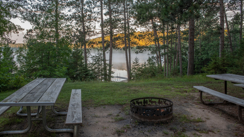 Picnic tables and a firepit overlooking a lake through trees