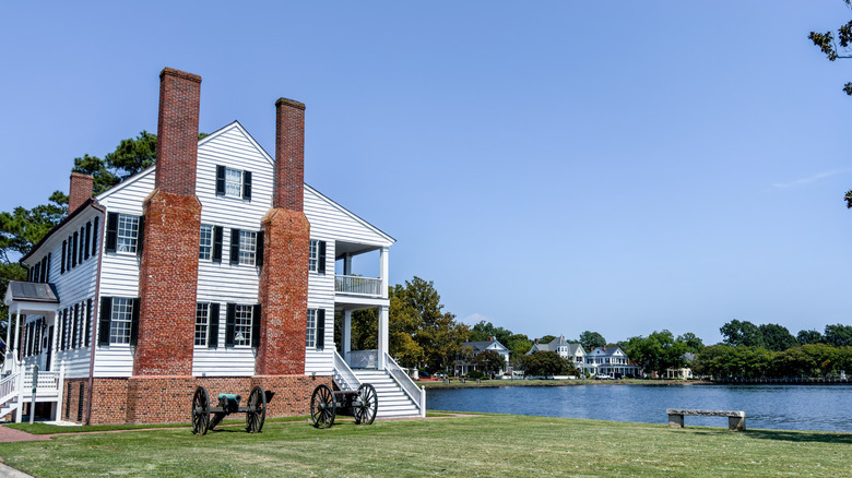 White building with two brick chimneys on a waterfront with two old canons in front.
