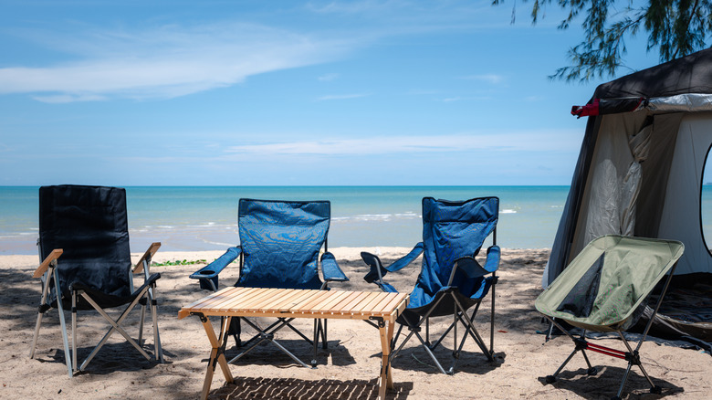 Beachfront campsite, Empty chairs, picnic table, and a tent under the summer sun.