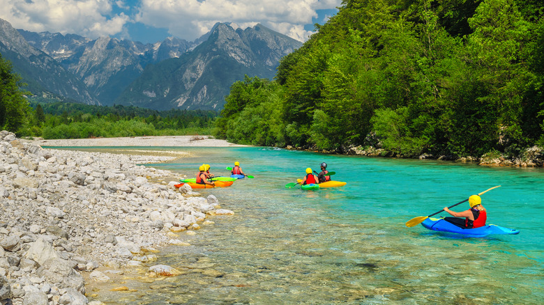 A group of kayakers on a turquoise river with mountains and green forests
