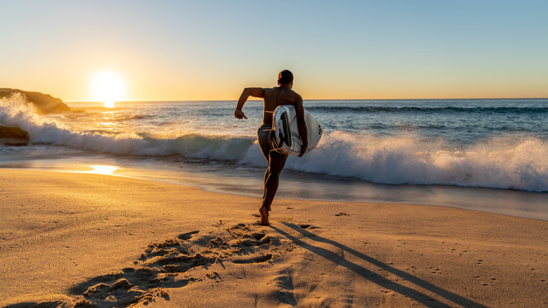 Surfer running into the water carrying his board with a beautiful sunrise