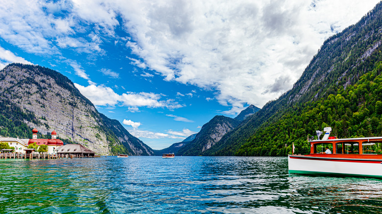 A red and white boat heads towards St. Bartholomä Church on Lake Königssee surrounded by mountains in Berchtesgaden National Park in Germany