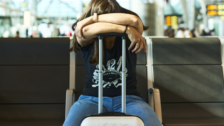 Frustrated airport traveler leaning on suitcase handle