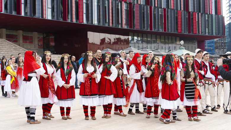 a group of girls and boys dressed in traditional red, white and black Albanian costumes