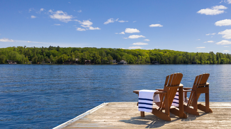 Two Adirondack chairs with neatly folded beach towels sit on a wooden dock