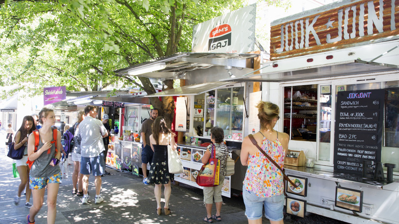 People walking and standing near food trucks on sunny day