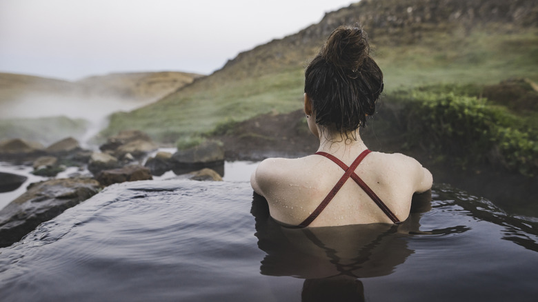 A woman looks out over a valley from a hot springs pool