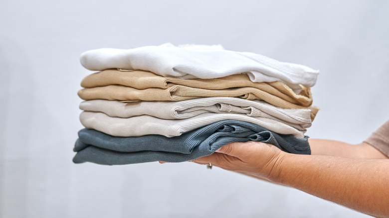 A set of hands holding a pile of light colored shirts folded
