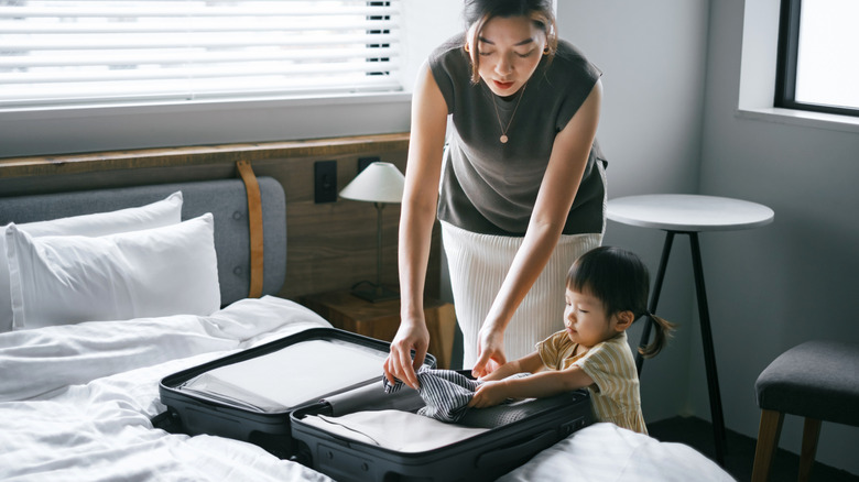 A woman and child pack a suitcase in a bedroom