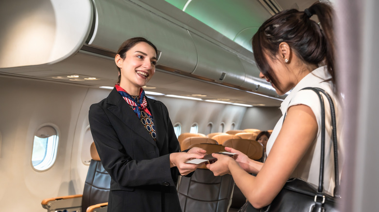 A flight attendant checking a young woman's boarding pass.