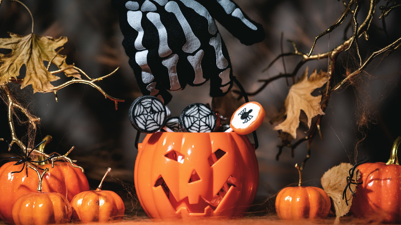 A skeleton hand reaching for a festive pumpkin candy bowl