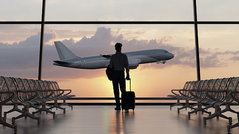 Silhouette of a man walking in the airport as the plane takes off during sunset