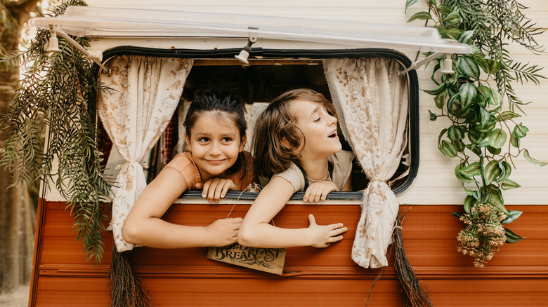 two children hanging out window of retro travel trailer