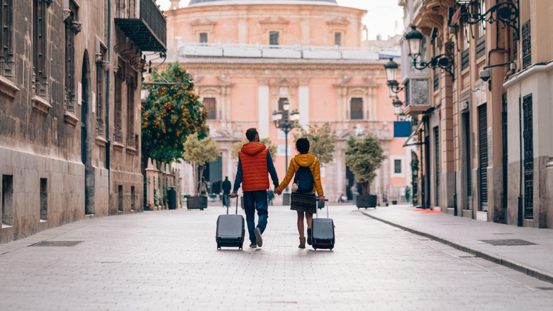 couple holding hands with luggage on street
