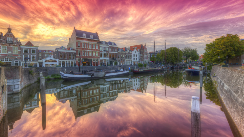A canal reflects old buildings and a blazing sunset in Delft, Netherlands