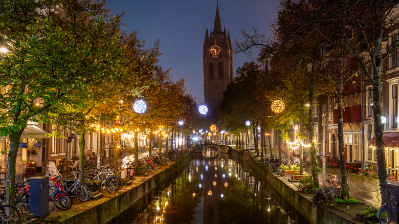A clock tower, bicycles, and decorative lights are all reflected in the water in Delft, Netherlands