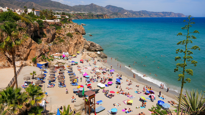 People lying on Playa de la Calahonda surrounded by rocky outcrops and palm trees near Nerja, Spain
