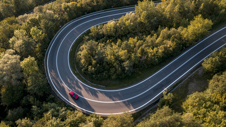 Aerial view of red car on road winding through forest