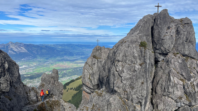 Two hikers in the mountains with a cross on top of a peak