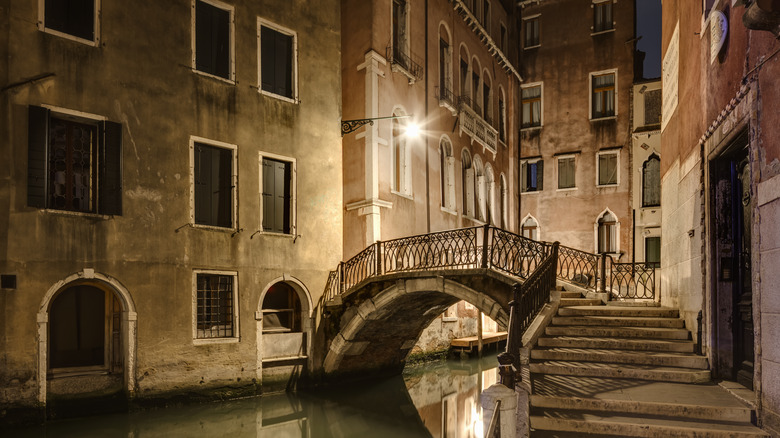 An empty street along a canal with a bridge at night in Venice