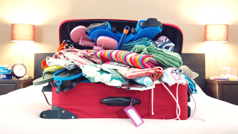 Overpacked luggage filled with clothing on a bed