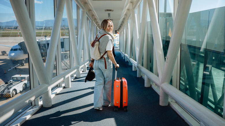 A woman walking on the boarding bridge toward an airplane with orange luggage