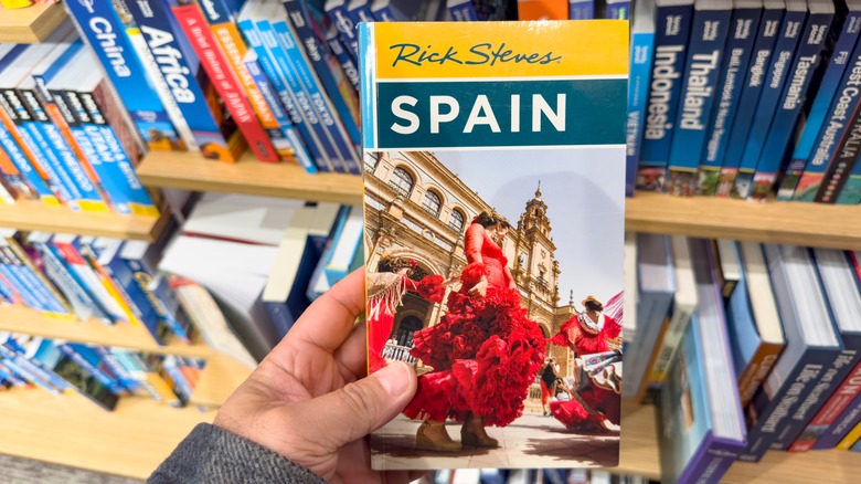A view of a hand holding a Rick Steves travel book, at the book store