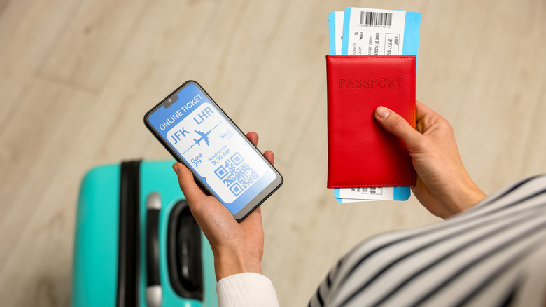 A traveler holds a passport, plane tickets, and a phone with QR code