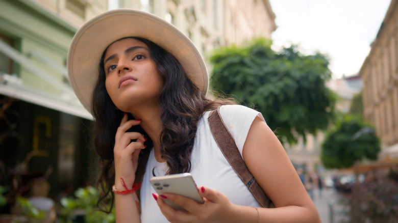 An anxious looking woman holds her phone and cranes her neck on the street