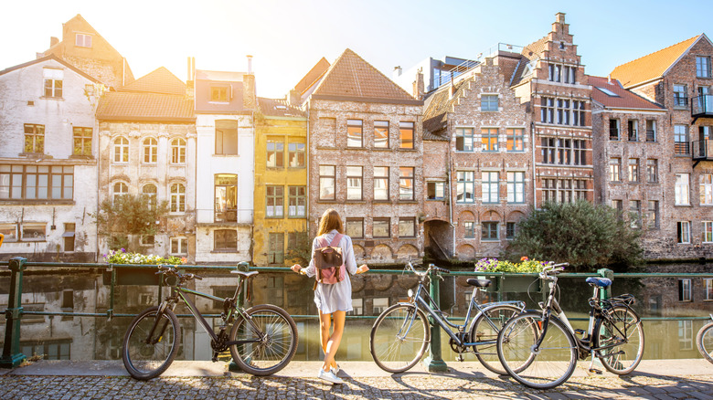 Sunrise view of woman on the canal with old buildings standing near the bicycles in Ghent