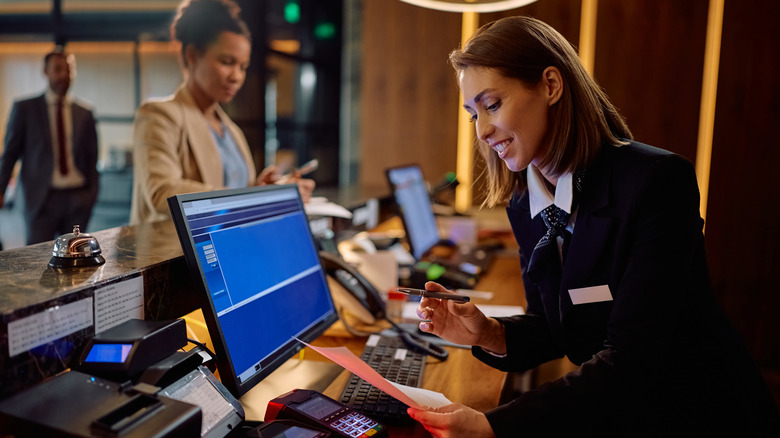 A hotel manager fills out registration documents during guest check-in at a reception desk.