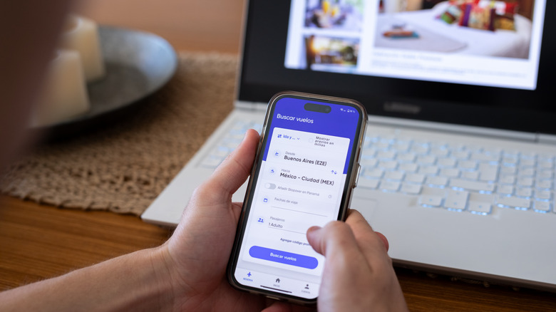 person searching for flights using mobile phone and laptop