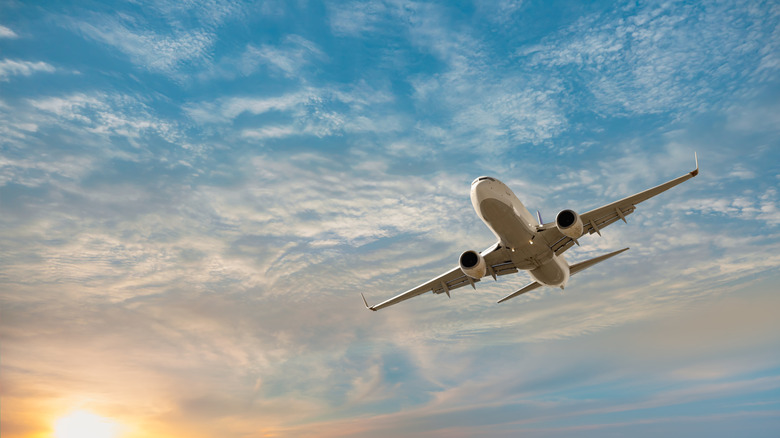 Airplane flying in a lightly cloudy blue sky at sunset