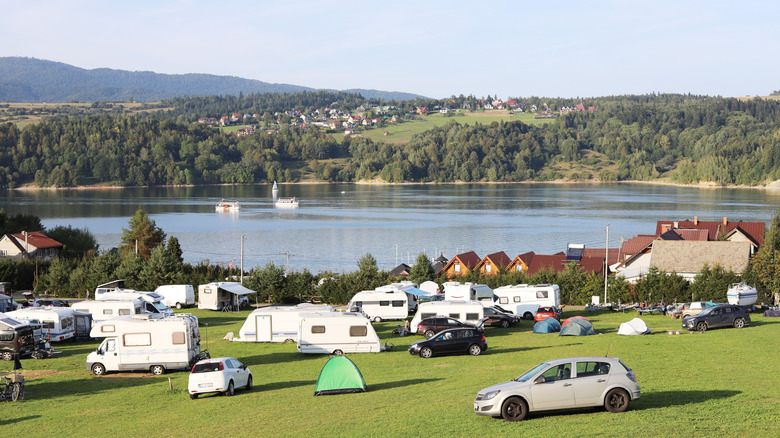 A campsite with a lake and hills in the background with cars and trailers parked