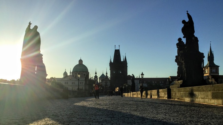 sun behind a statue, medieval buildings, pavement