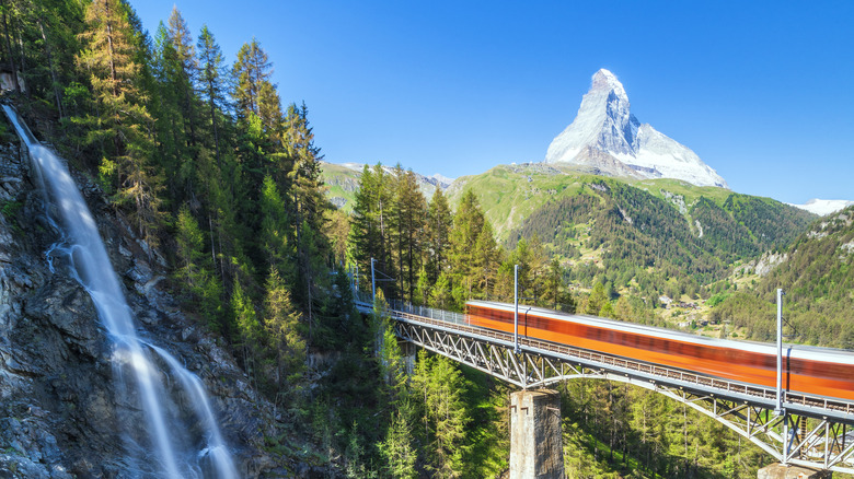 A mountain train crossing a valley bridge with the peak in the background