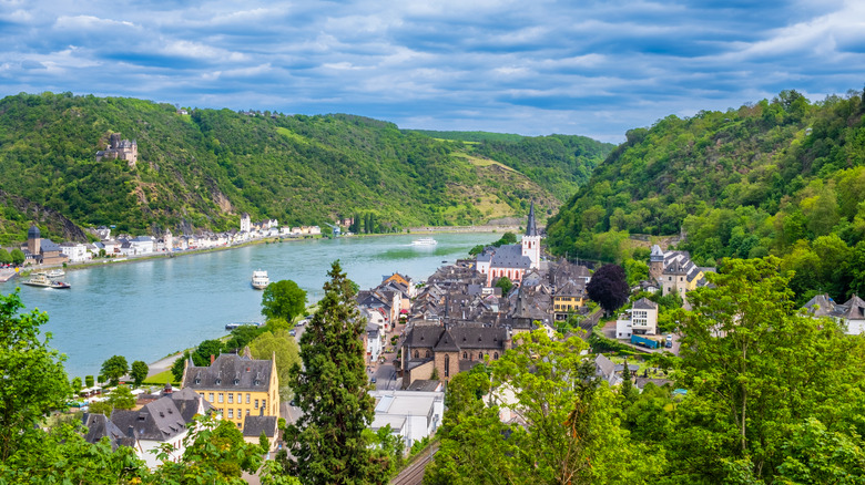 A picturesque village and castle along the Rhine River, surrounded by hills