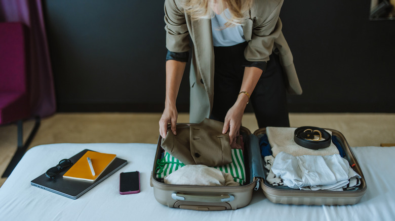 woman placing clothing items into a suitcase