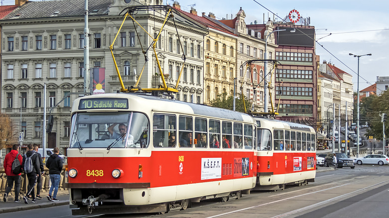 red tram on a road, pedestrians, buildings