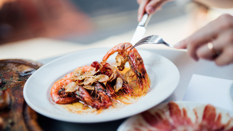 A plate with grilled prawns being picked up by a knife and fork