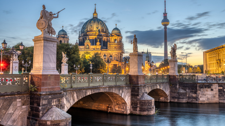 A stone multi-arched bridge adorned with statues and a domed cathedral in the background
