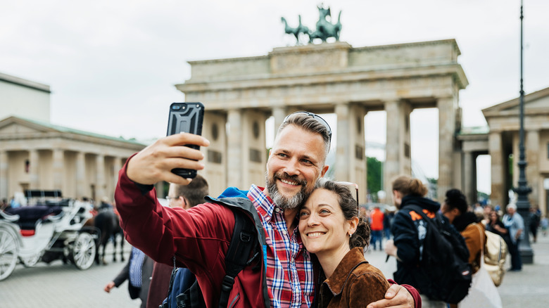 A man and woman take a selfie in front of the Brandenburg Gate in Berlin