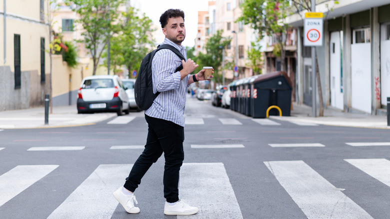 A young man crossing a crosswalk holding a cup of coffee