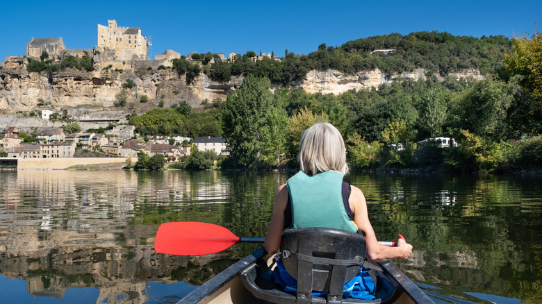 A woman kayaking on the Dordogne River past historic sandstone villages